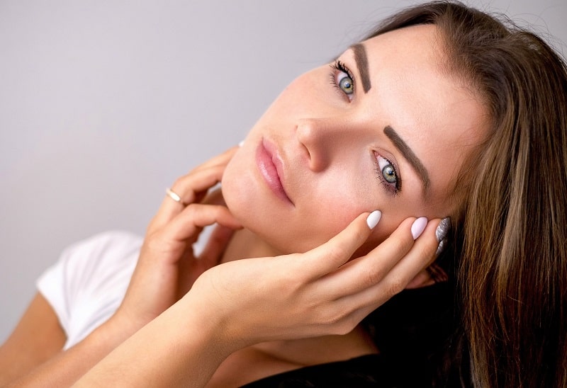 Non-Surgical Body Treatments Portrait of a Woman with her Head Tilted to One Side and Her Hands Against Her Face